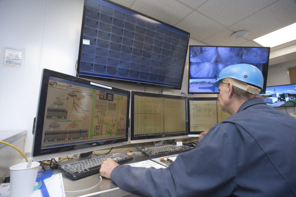A feed mill worker sits in front of mulitple screens while monitoring inventory levels.