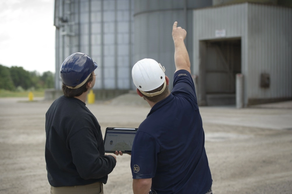 Two employee's assessing a silo and analysing details about it on a tablet.